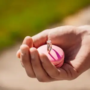 Une personne tient un macaron rose avec une bague en diamant, symbolisant une célébration ou une occasion spéciale.